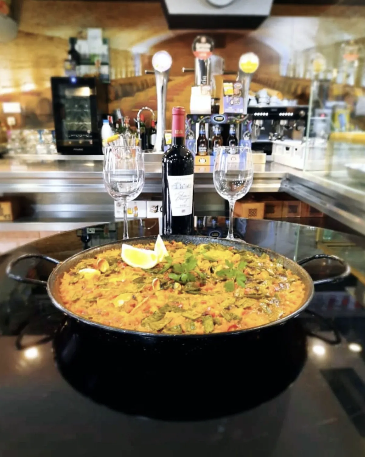 Paella de la casa servida en la barra, con vino y dos copas