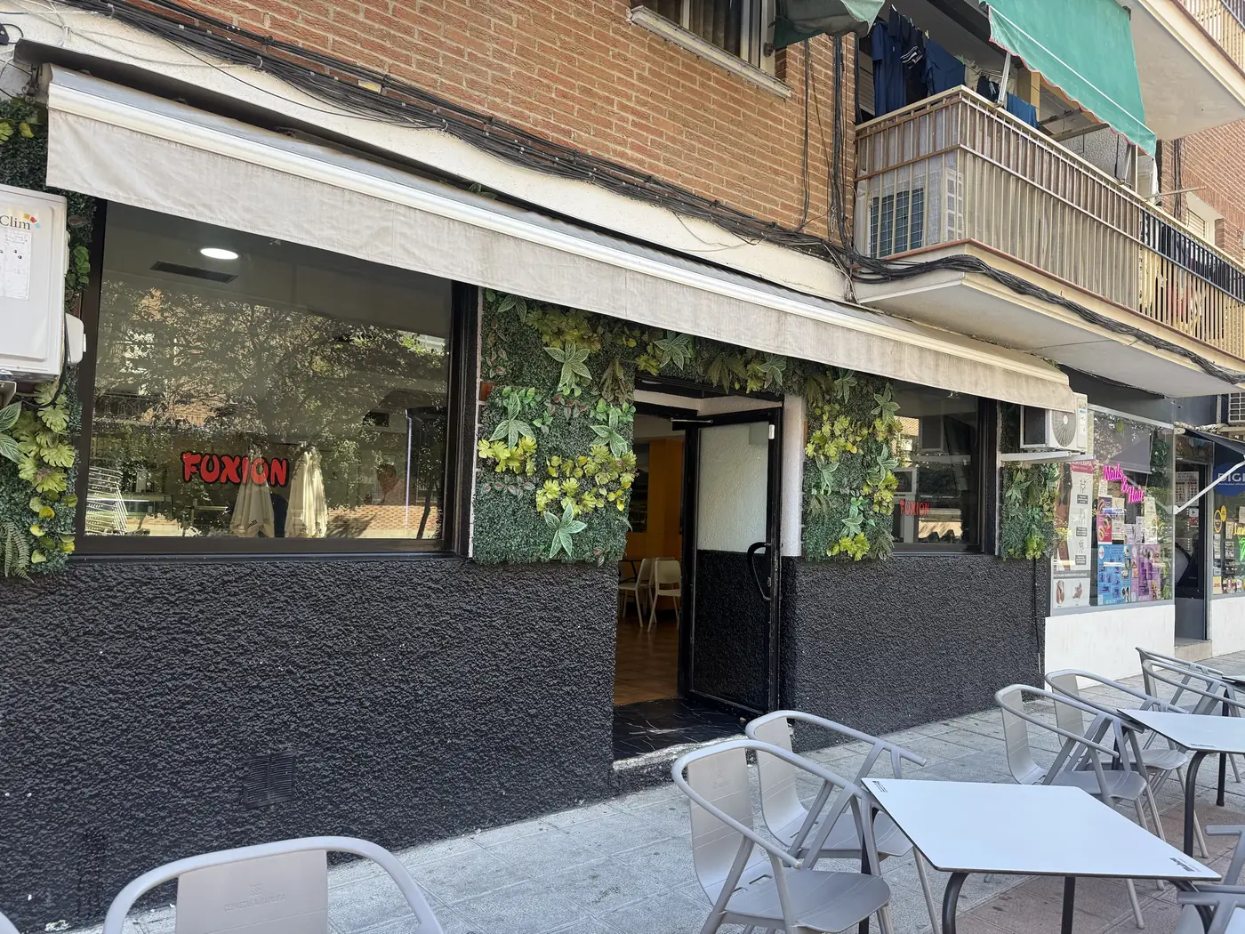 Entrada al local con la fachada de plantas y el rótulo Fuxion